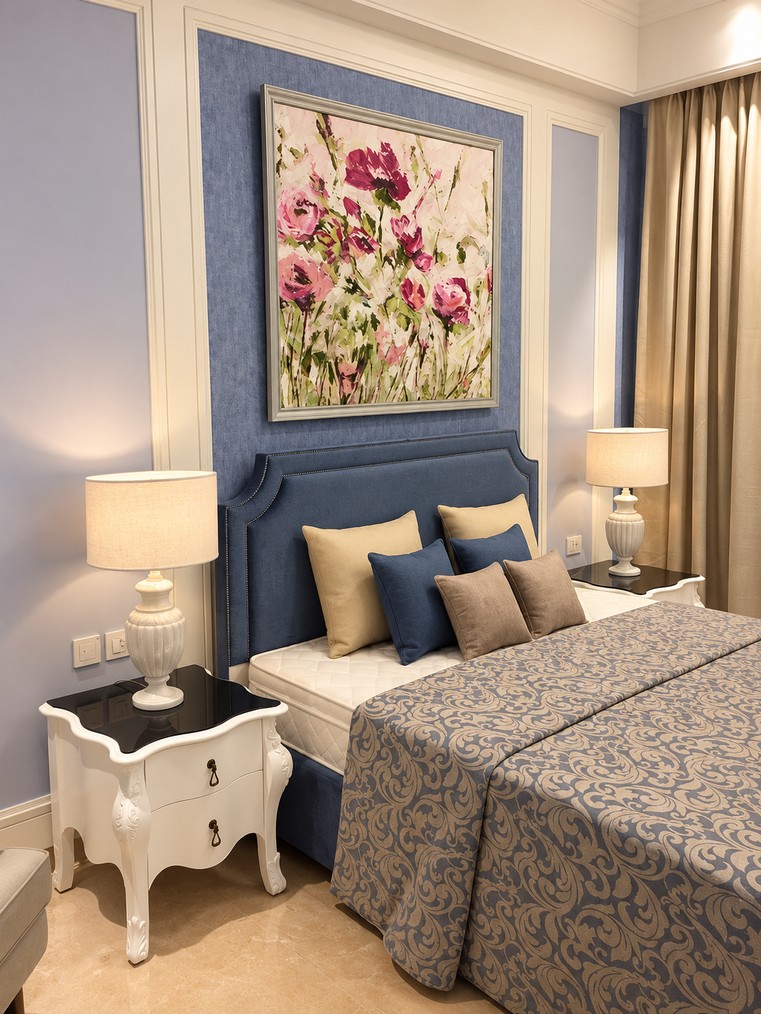 Bedroom with blue upholstered headboard and floral artwork